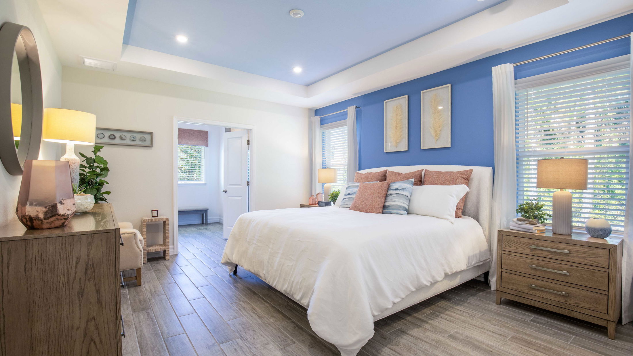 Modern bedroom with blue accent wall, stylish decor, white bedding, and natural light from large windows.