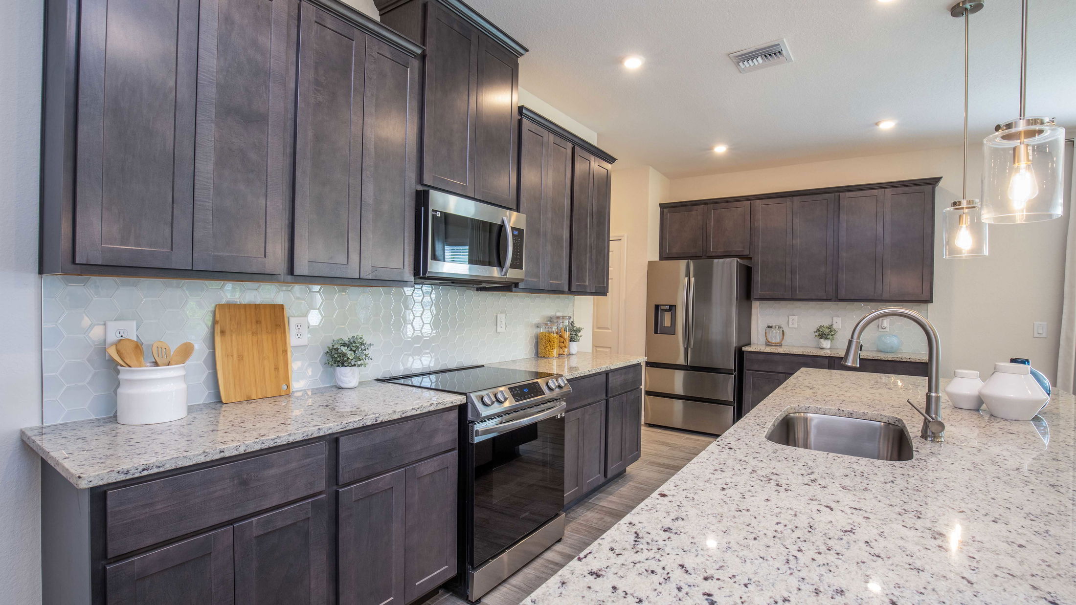 Modern kitchen with dark wooden cabinets, stainless steel appliances, and a granite countertop island with pendant lighting.