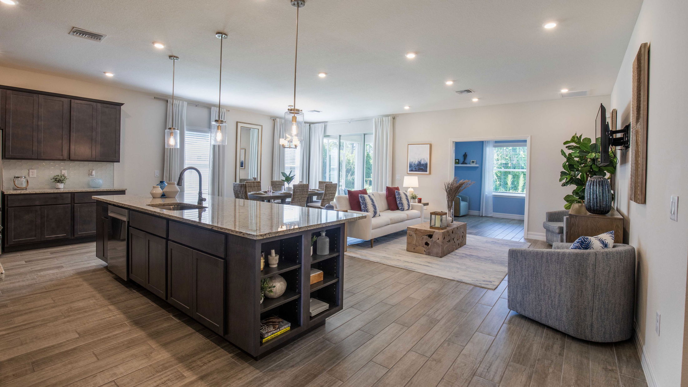 Modern open-concept living room and kitchen with wooden flooring, featuring a large island, stylish furniture, and ample natural light.