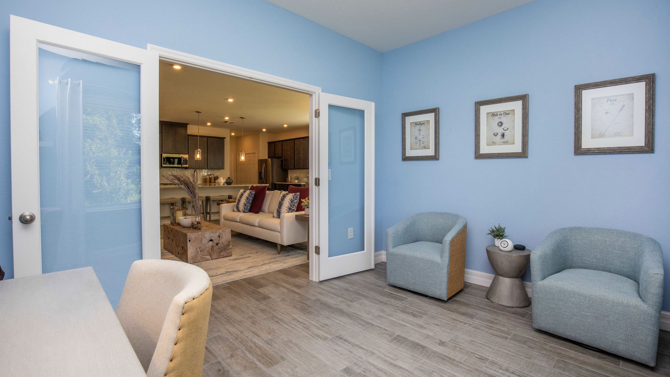Modern home office with blue walls and stylish seating, opening to a cozy living room and kitchen.