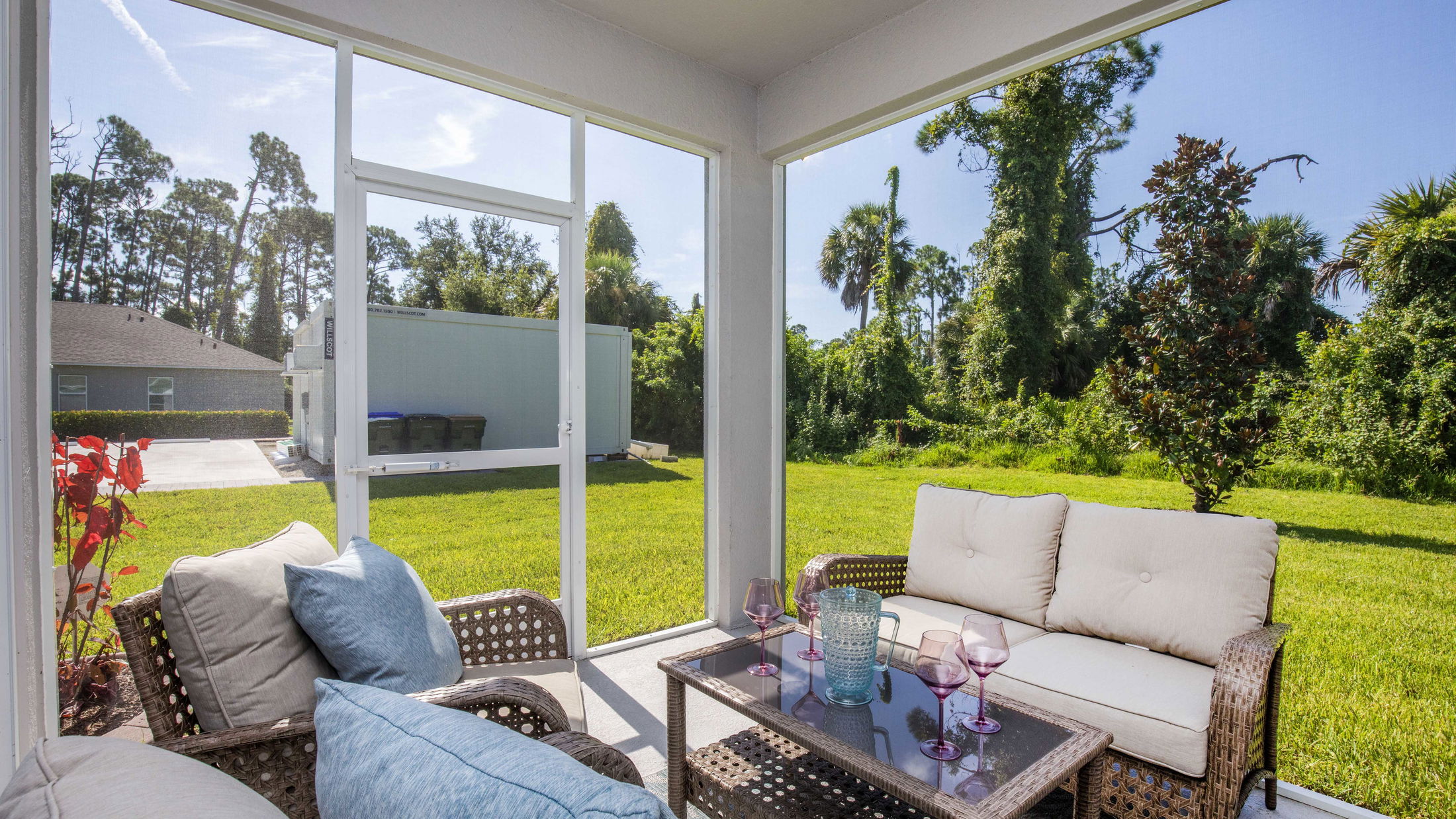 Spacious screened patio with wicker furniture and glass-topped table overlooking a lush green backyard.