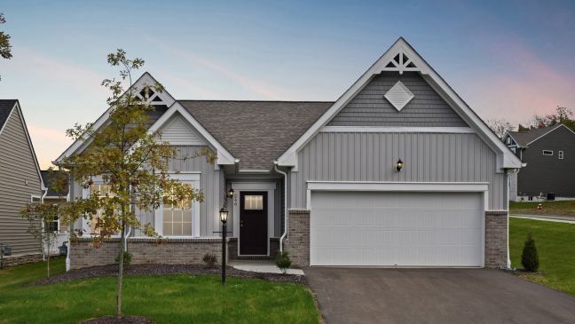 Modern suburban house with gray siding, gable roof, and attached garage at sunset.
