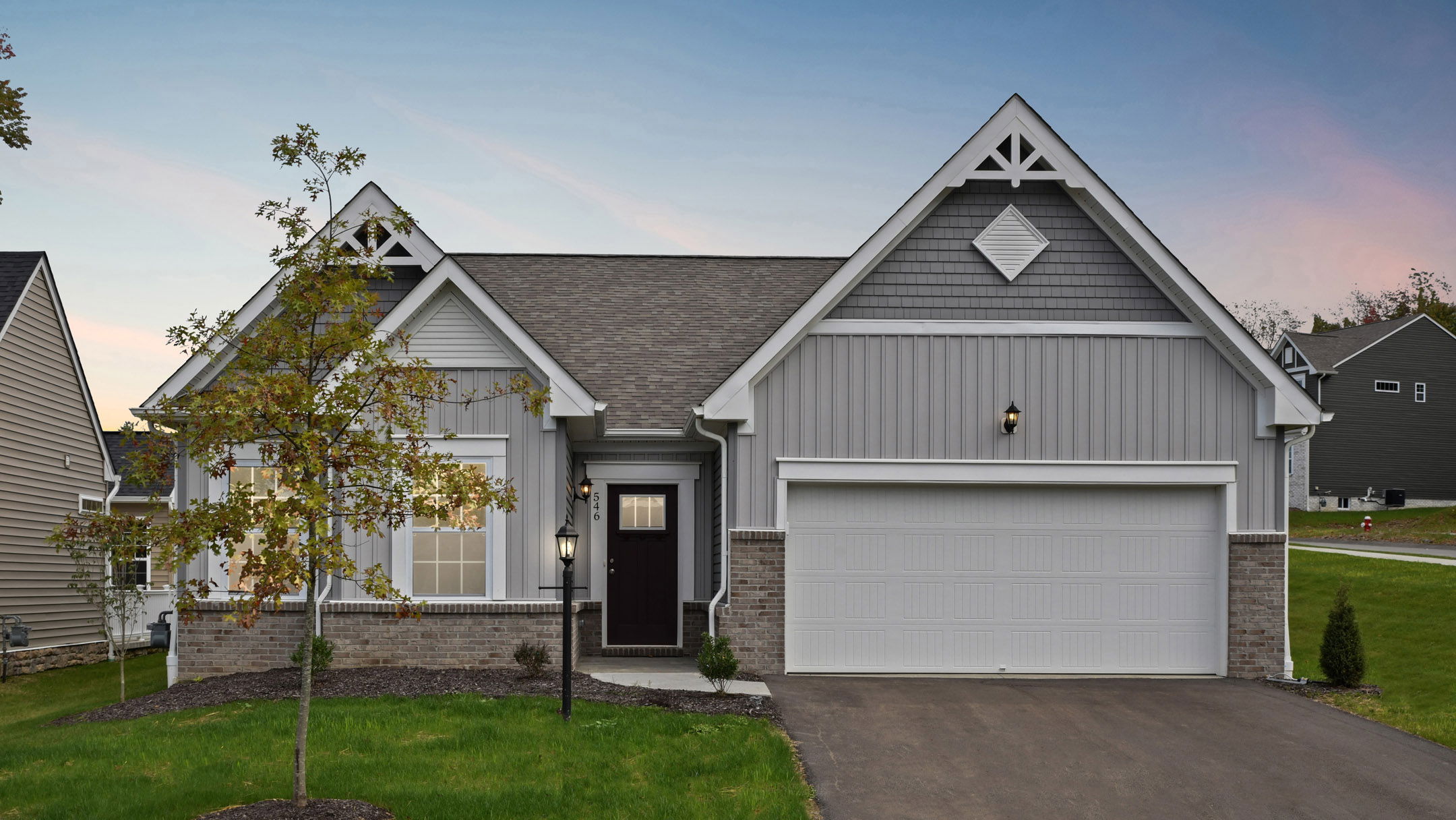 Gray single-story suburban house with a gable roof, large garage, and well-maintained front yard at dusk.