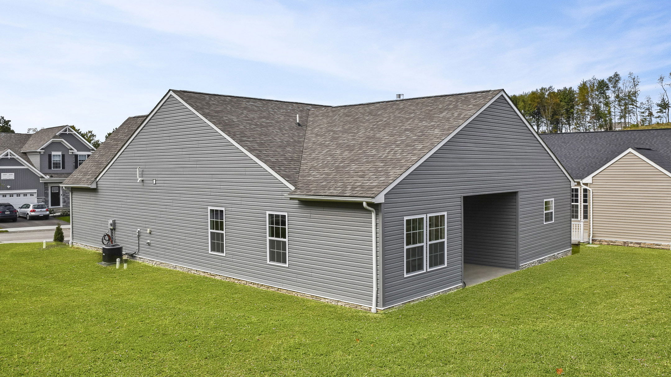 Single-story gray house with a shingled roof and spacious backyard, situated in a suburban neighborhood.