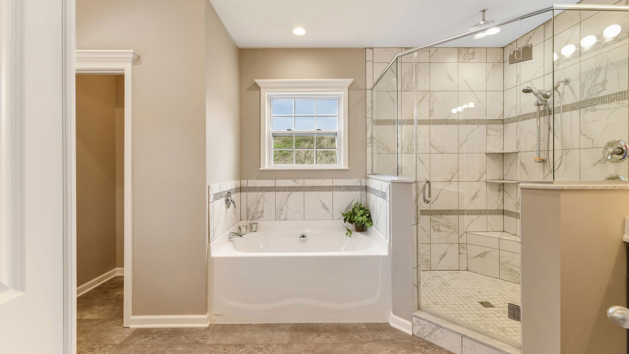 Elegant bathroom with a white bathtub and a modern glass-enclosed marble shower under warm lighting.