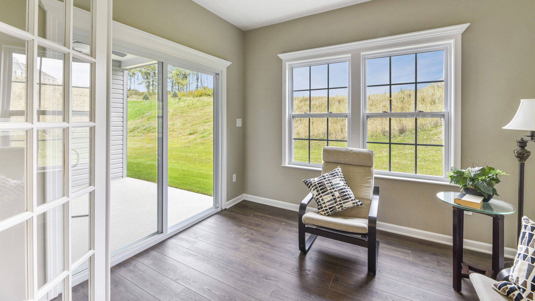 Bright sunroom interior with wooden flooring, a comfortable chair, and glass sliding doors leading to a green lawn.