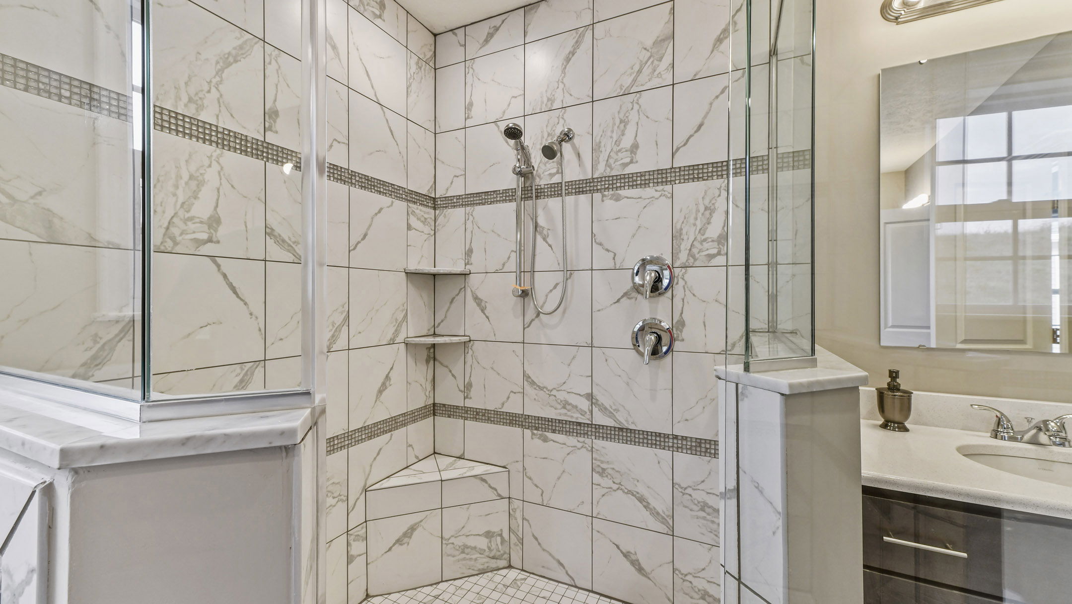 Luxurious bathroom showcasing a marble-tiled walk-in shower with dual shower heads and glass enclosure, adjacent to a modern sink and vanity.
