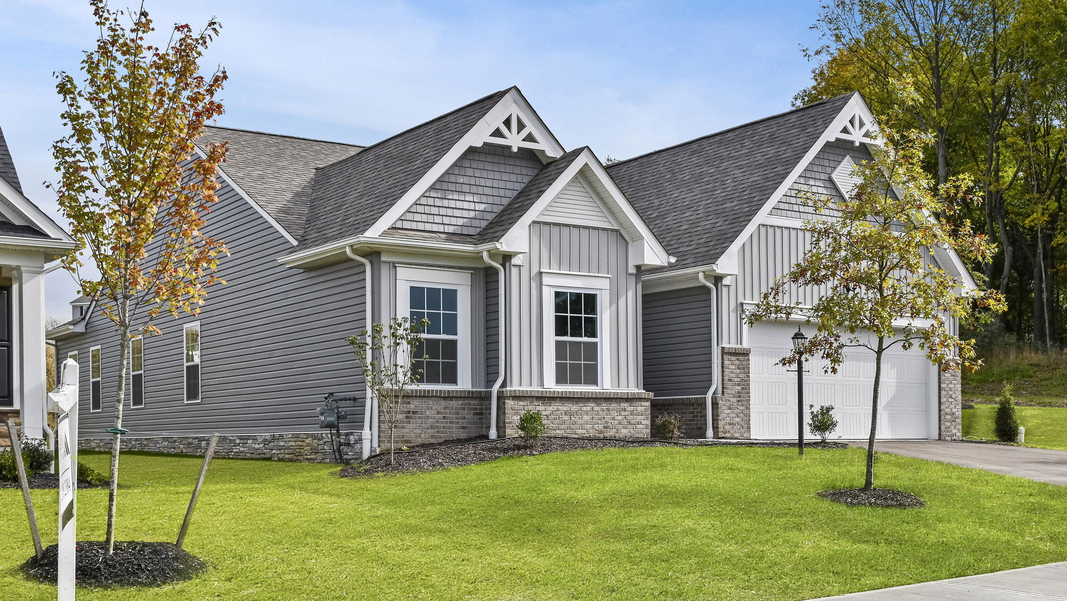 Modern gray suburban house with gabled roof, white trim, and landscaped front yard on a sunny day.