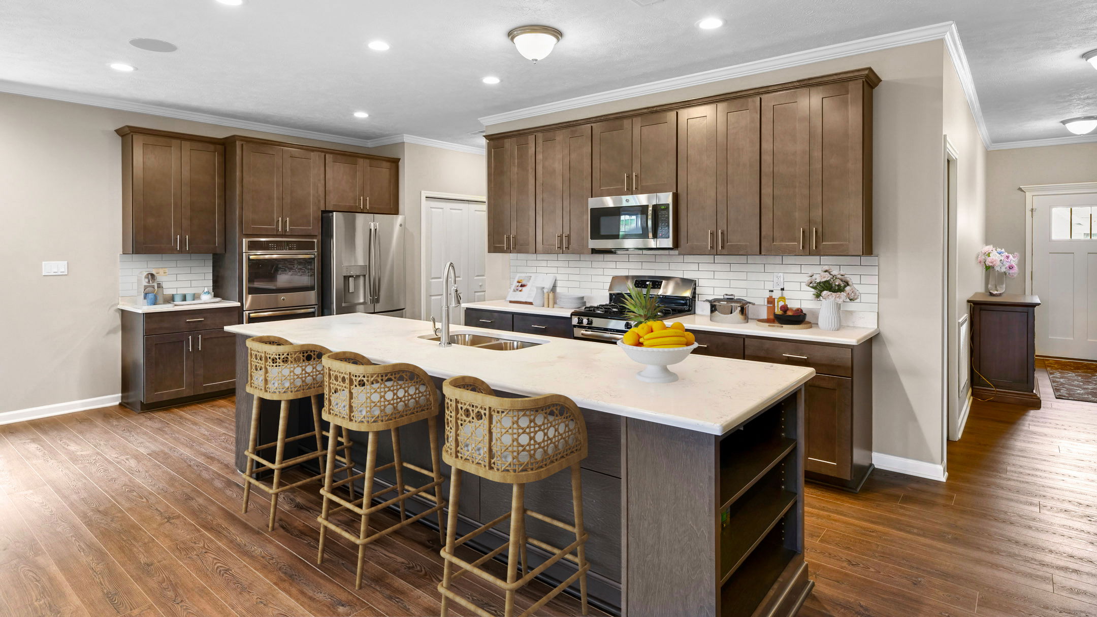 Modern kitchen with dark wood cabinets, stainless steel appliances, and an island featuring wicker barstools and a fruit bowl centerpiece.