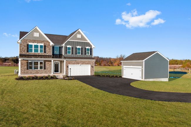 Modern two-story brick and siding house with a detached garage on a spacious green lawn under a clear blue sky.