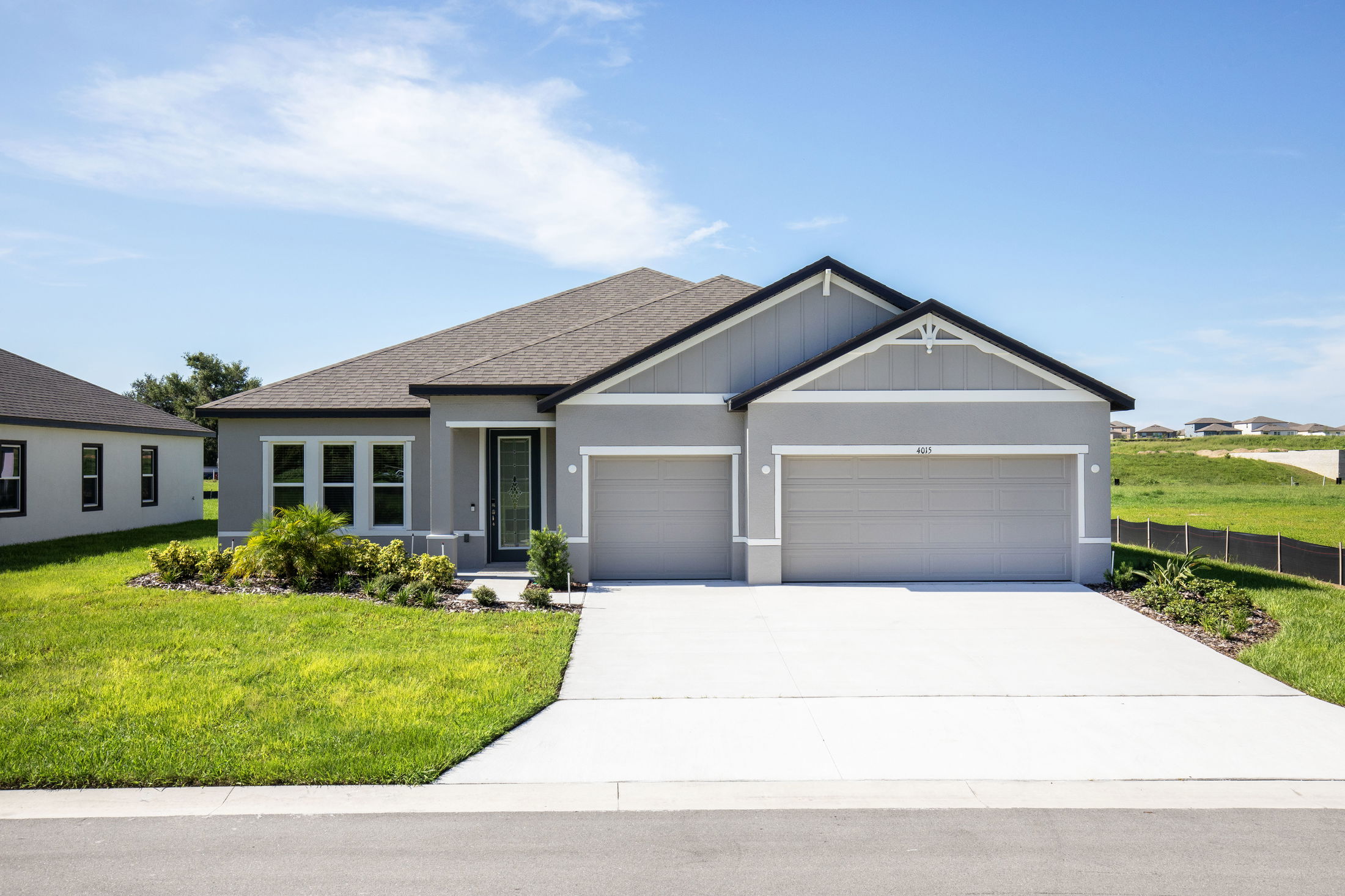 Modern single-story grey house with a well-maintained lawn and three-car garage under a clear blue sky.