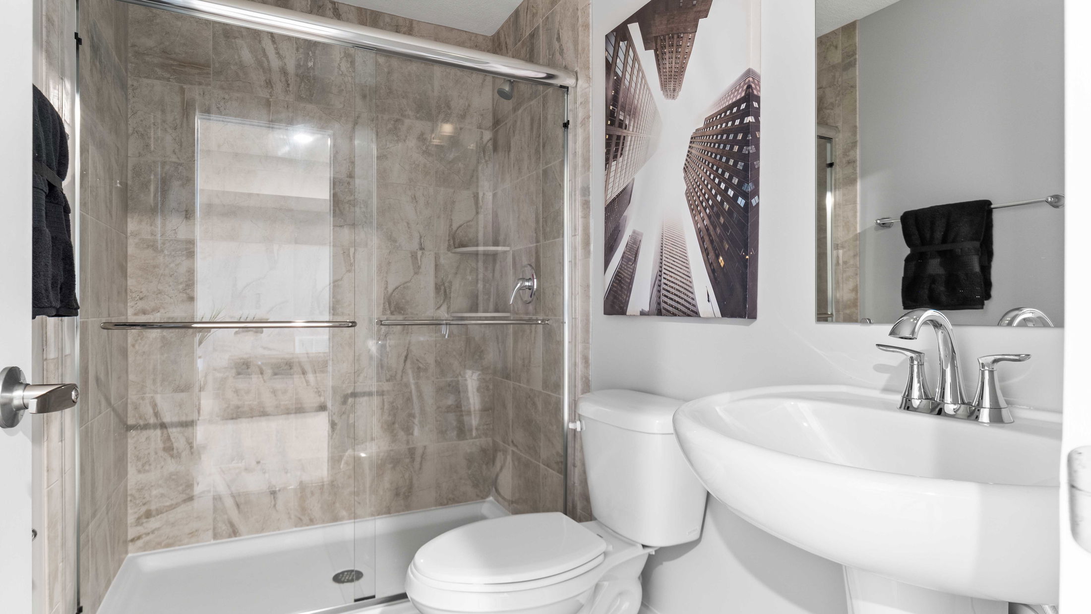 Modern bathroom interior with glass shower enclosure, white fixtures, and decorative wall art.