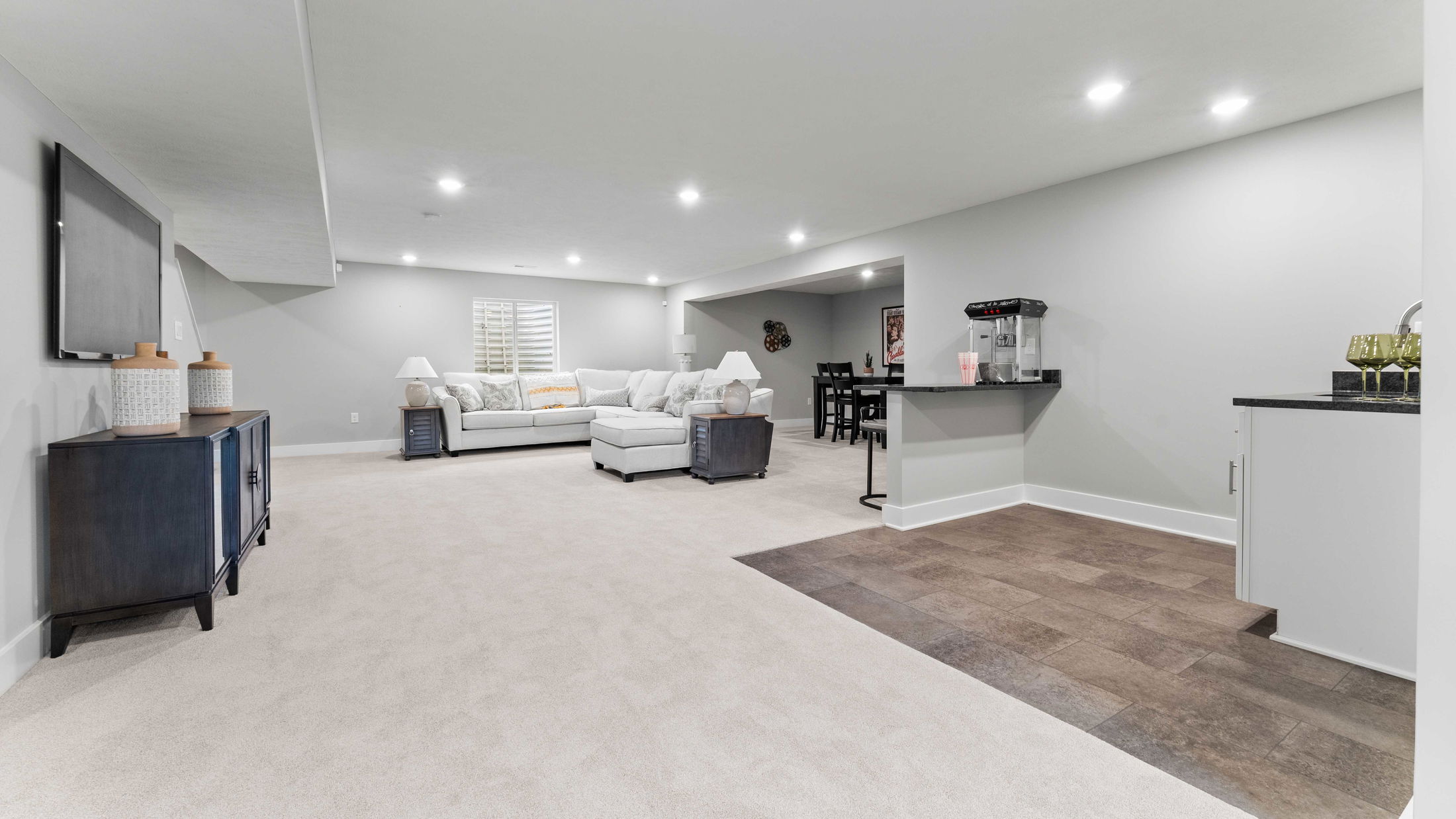 Modern basement living room featuring a cozy sectional sofa, entertainment center, and kitchenette with sleek decor.