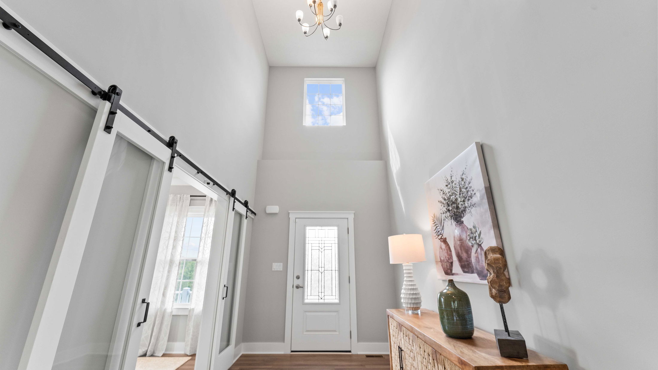 Modern home entryway featuring high ceilings, decorative glass front door, and sliding barn doors on the left.