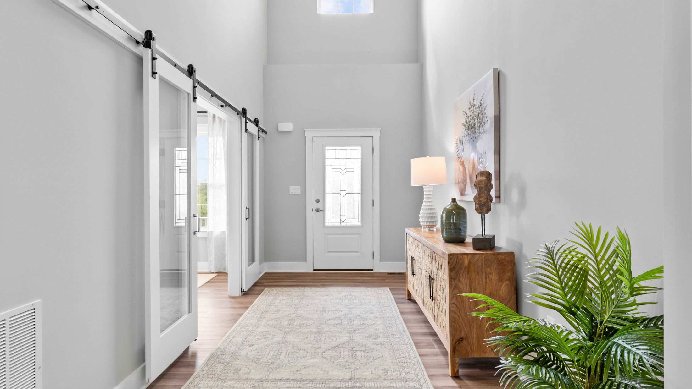 Modern home entryway with white walls, wooden sideboard, decorative lamp, and sliding doors.