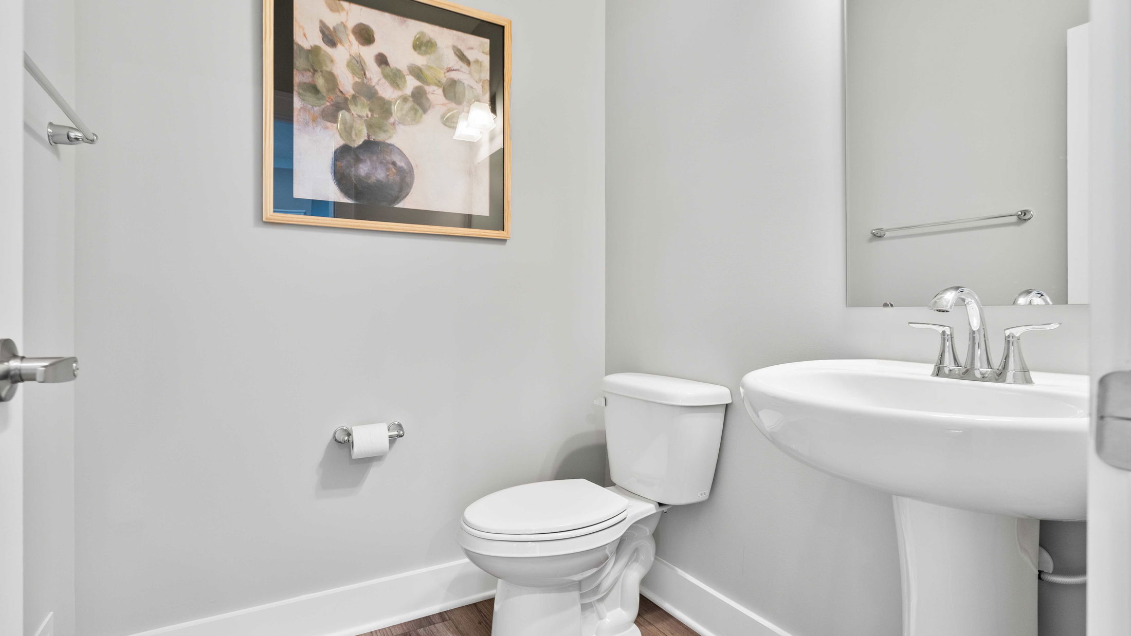 Minimalist bathroom interior featuring a white toilet, pedestal sink, and wall art on light gray walls.