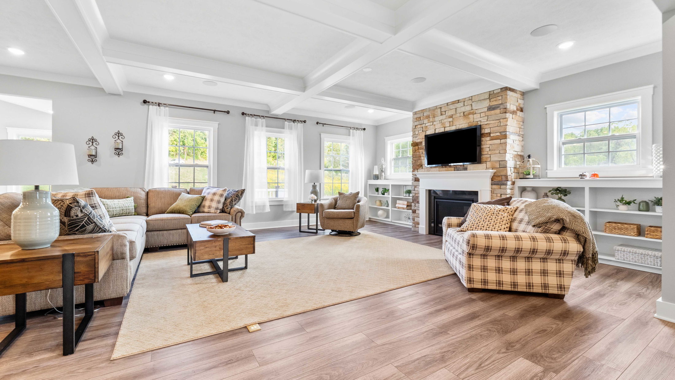 Spacious living room featuring a cozy sectional sofa, modern armchairs, stone fireplace, and large windows with natural light.