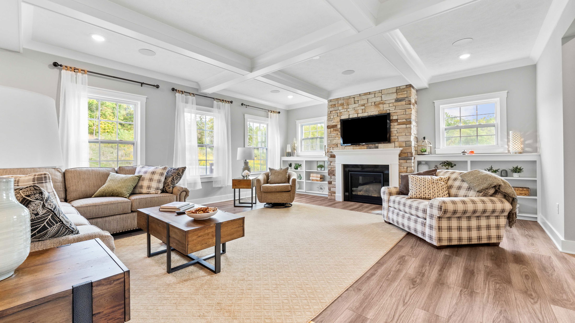 Spacious, modern living room featuring a stone fireplace, comfy seating, and natural light flooding through large windows.
