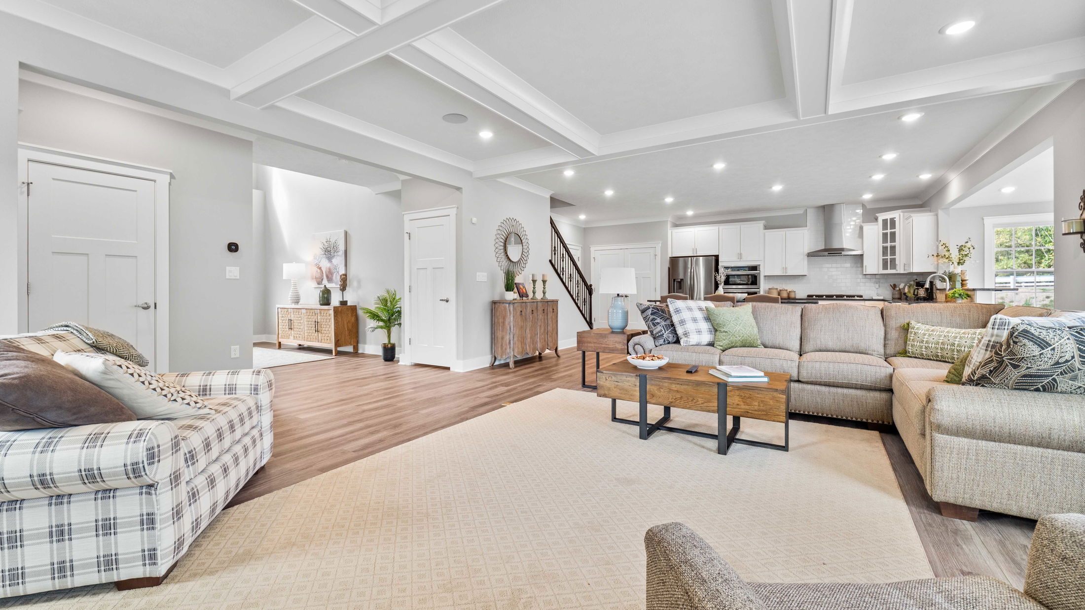 Spacious modern living room with L-shaped sofa, wooden coffee table, and open kitchen in the background, accented by cozy lighting and decorative elements.