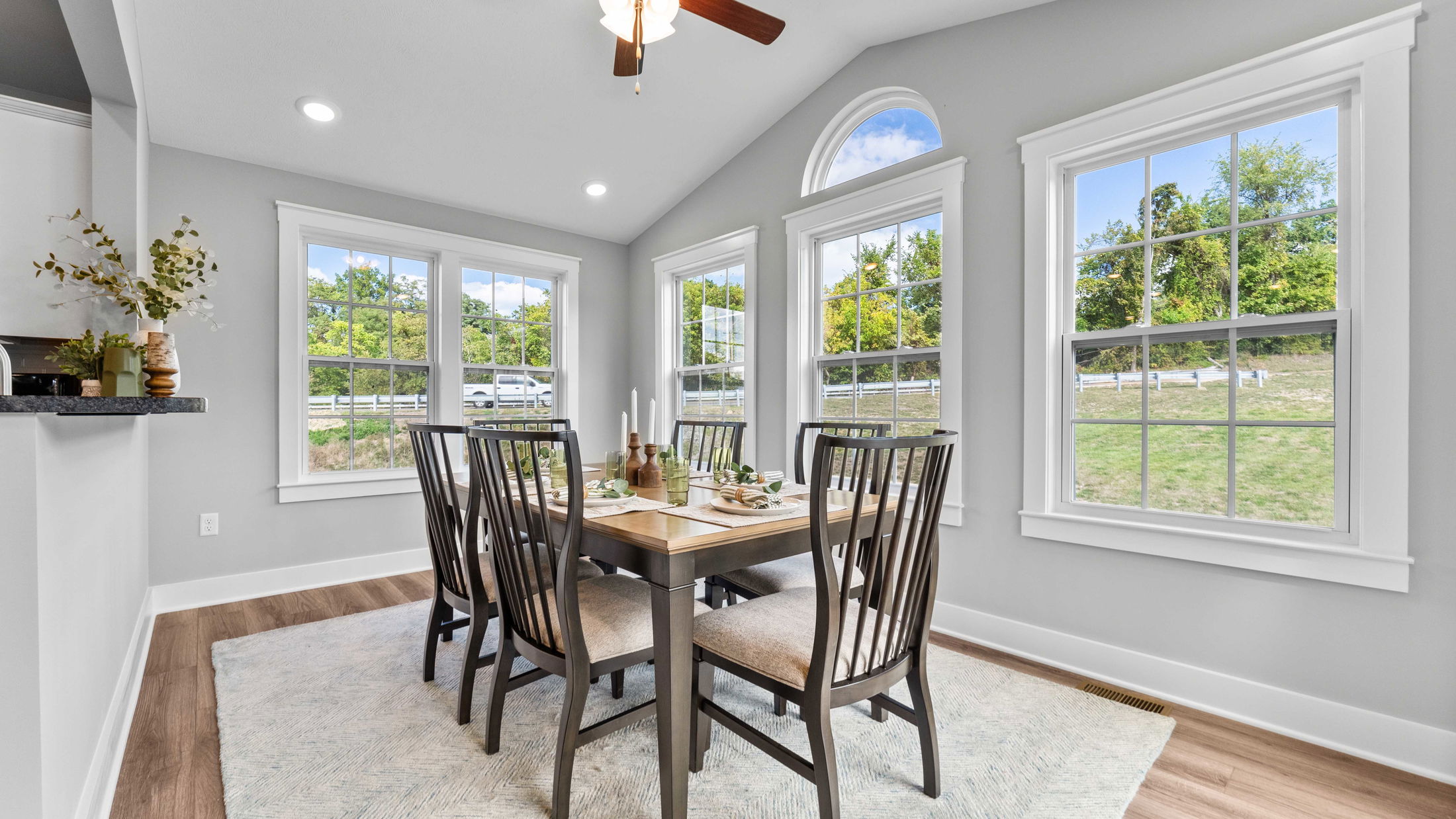 Bright dining room with large windows, wooden table set for six, and a view of the outdoors.