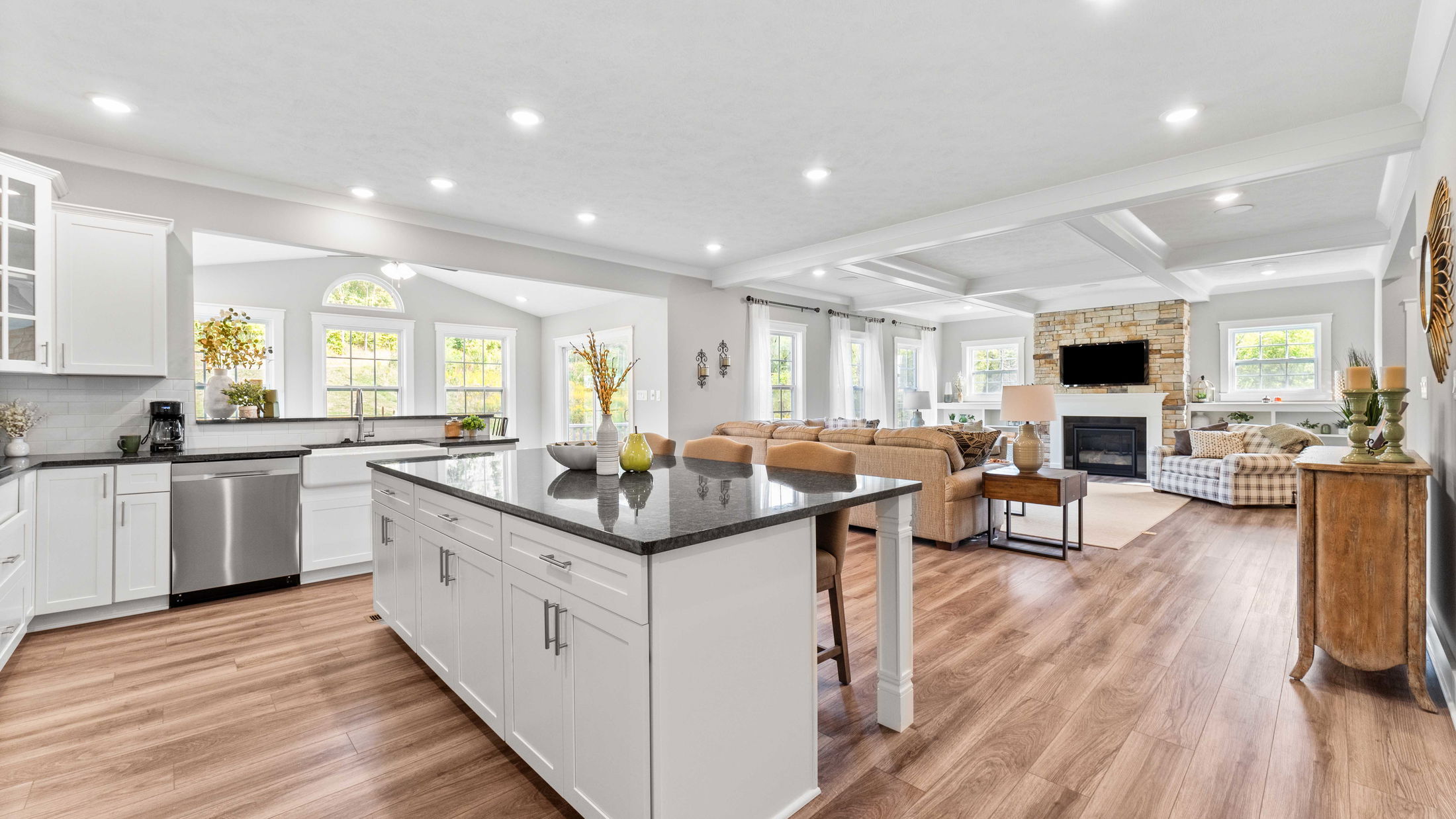 Bright and spacious open-concept kitchen and living room with modern furnishings and stone fireplace.