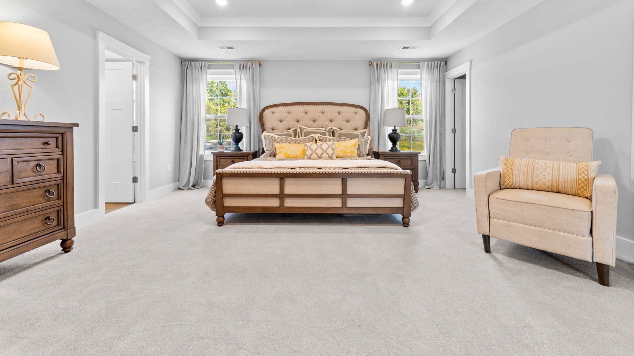 Elegant bedroom with a large upholstered bed, beige armchair, and wooden furniture, showcasing a cozy and sophisticated interior design.
