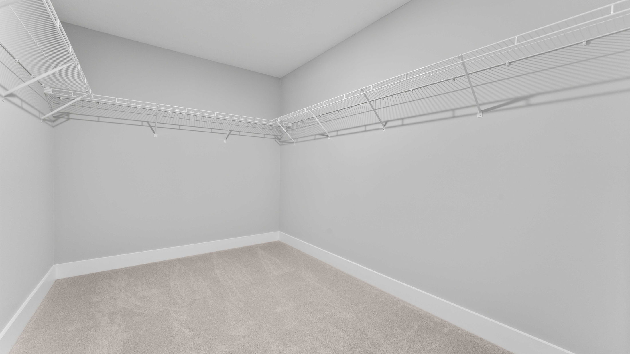 Empty walk-in closet with carpeted floor and wire shelving units on light gray walls.
