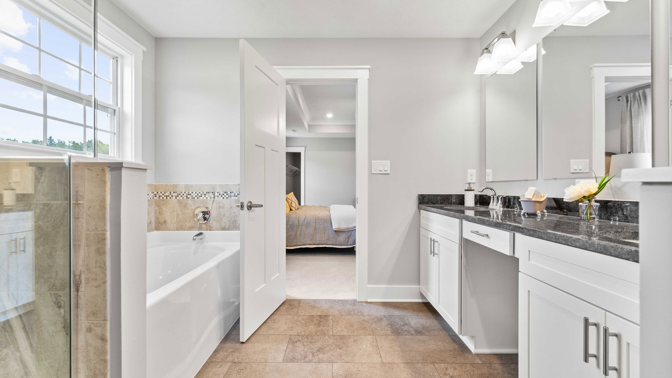 Modern bathroom with elegant fixtures, featuring a bathtub, large vanity, and view into a cozy bedroom.