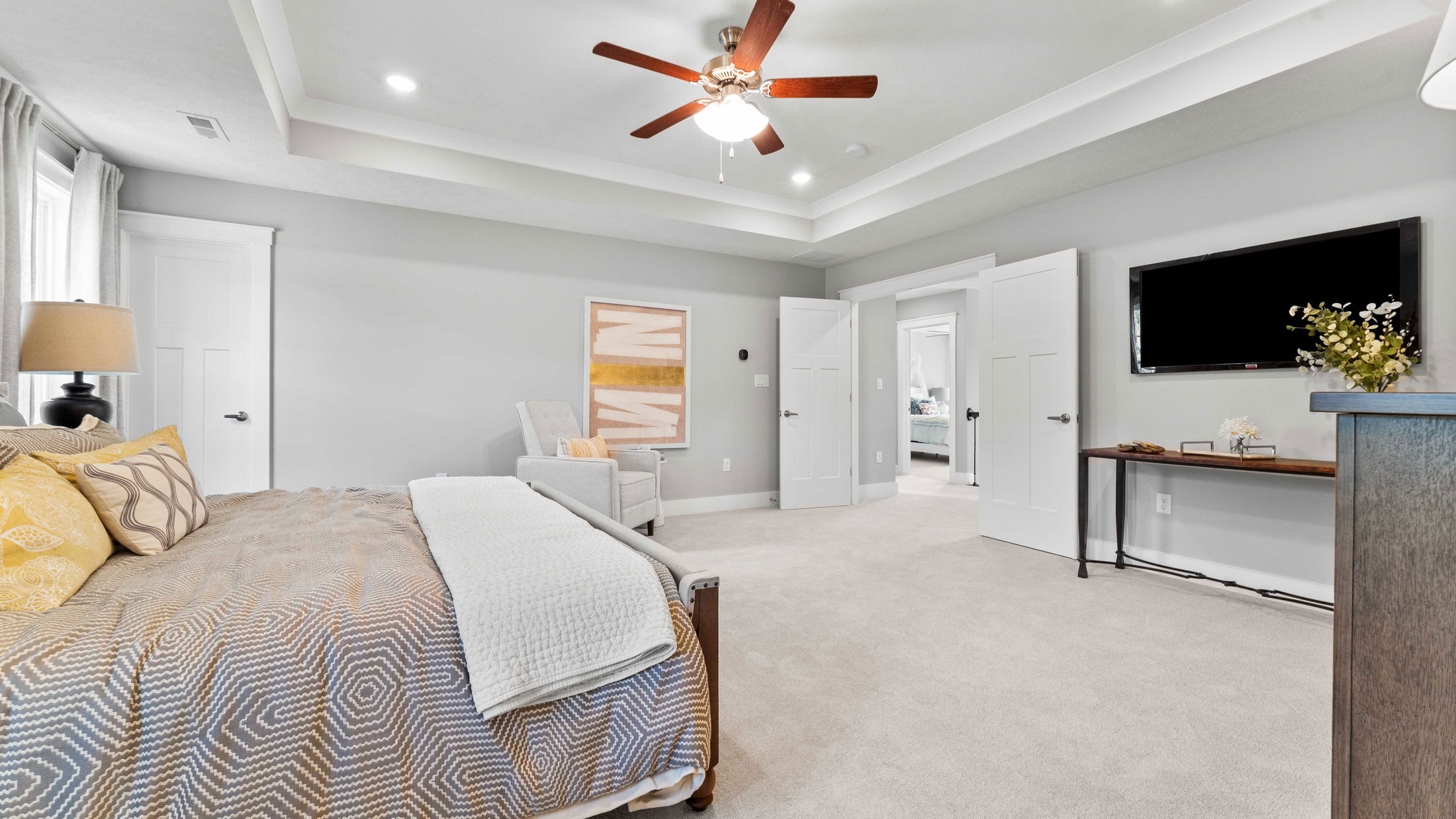 Modern, spacious bedroom with elegant decor featuring a comfortable bed, wall art, and a ceiling fan.