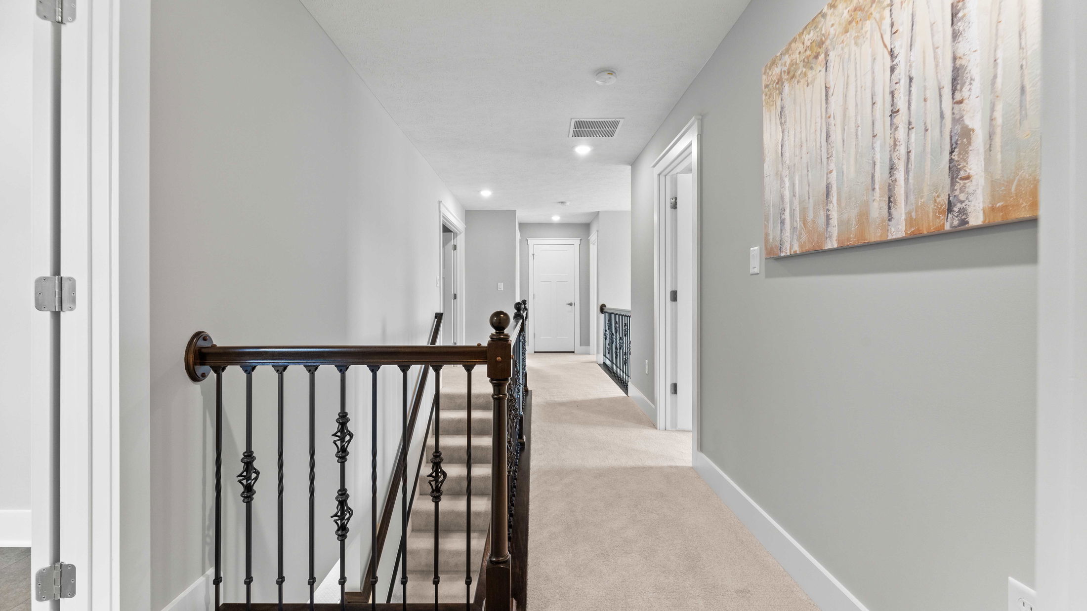 Modern upper hallway with light gray walls, a carpeted floor, and a decorative railing leading to multiple doors.