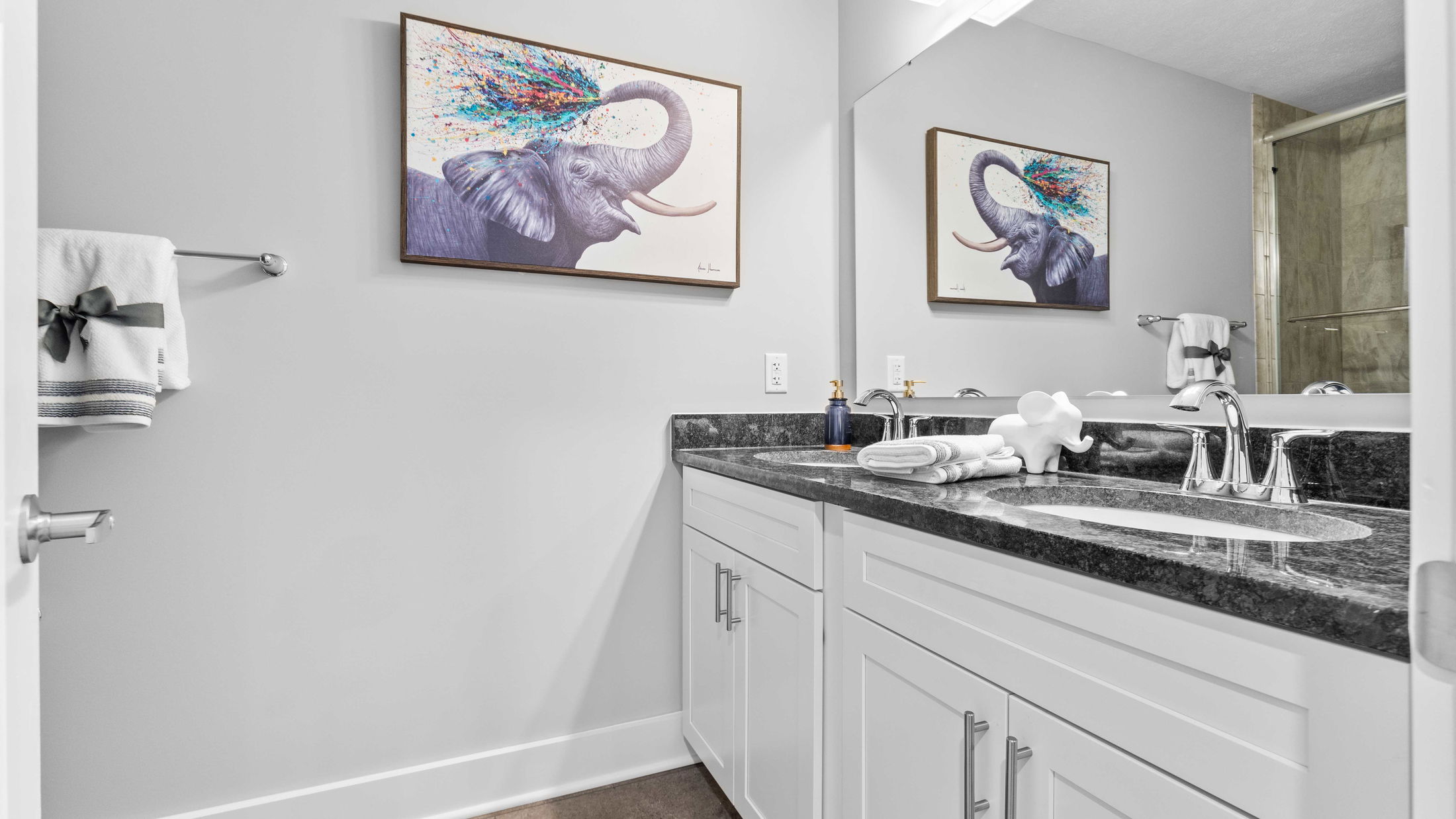 Modern bathroom with white cabinets, black granite countertops, and colorful elephant wall art reflecting in the mirror.