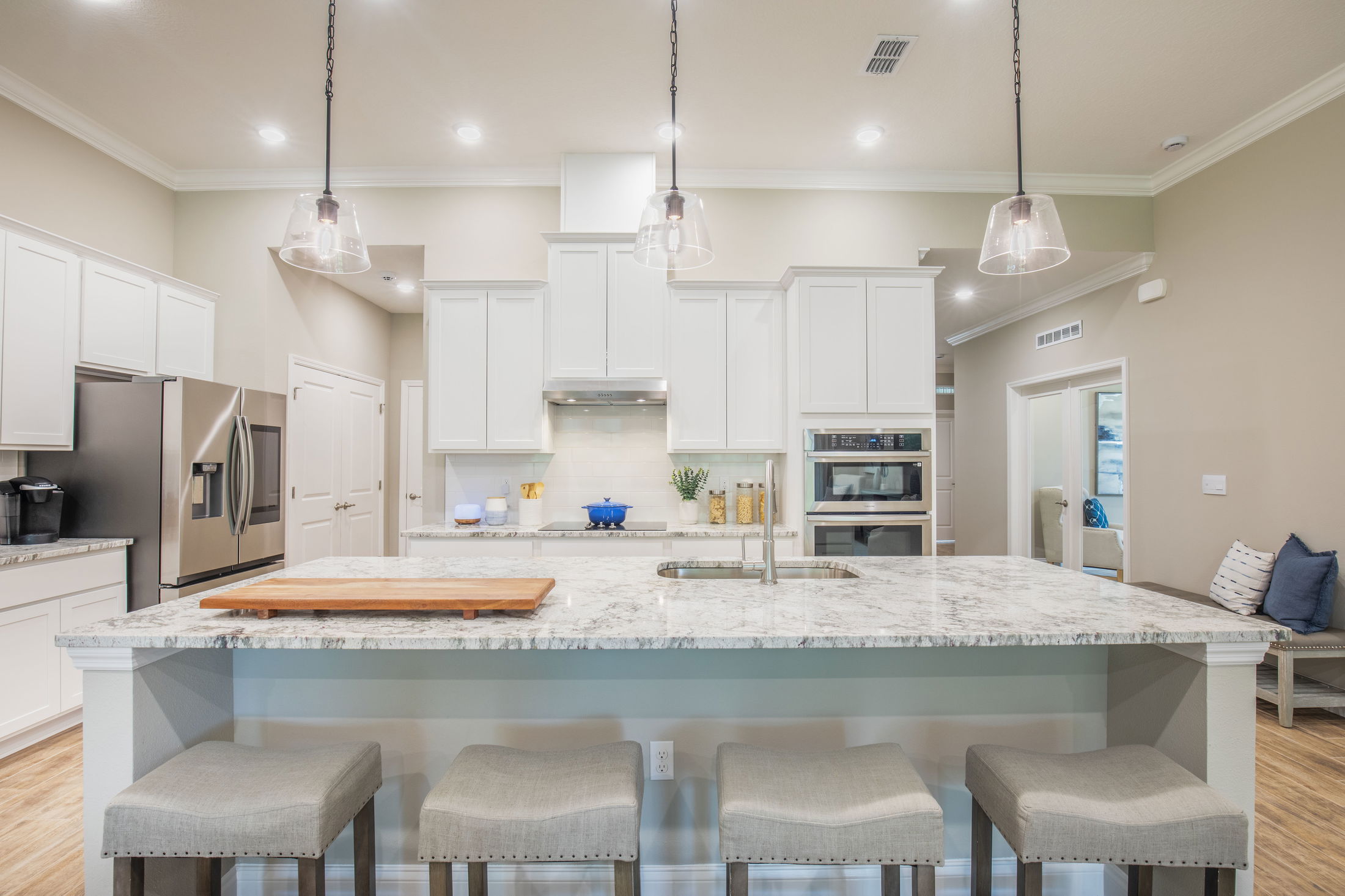 Modern kitchen with white cabinets, stainless steel appliances, and a spacious marble island with bar stools and pendant lighting.