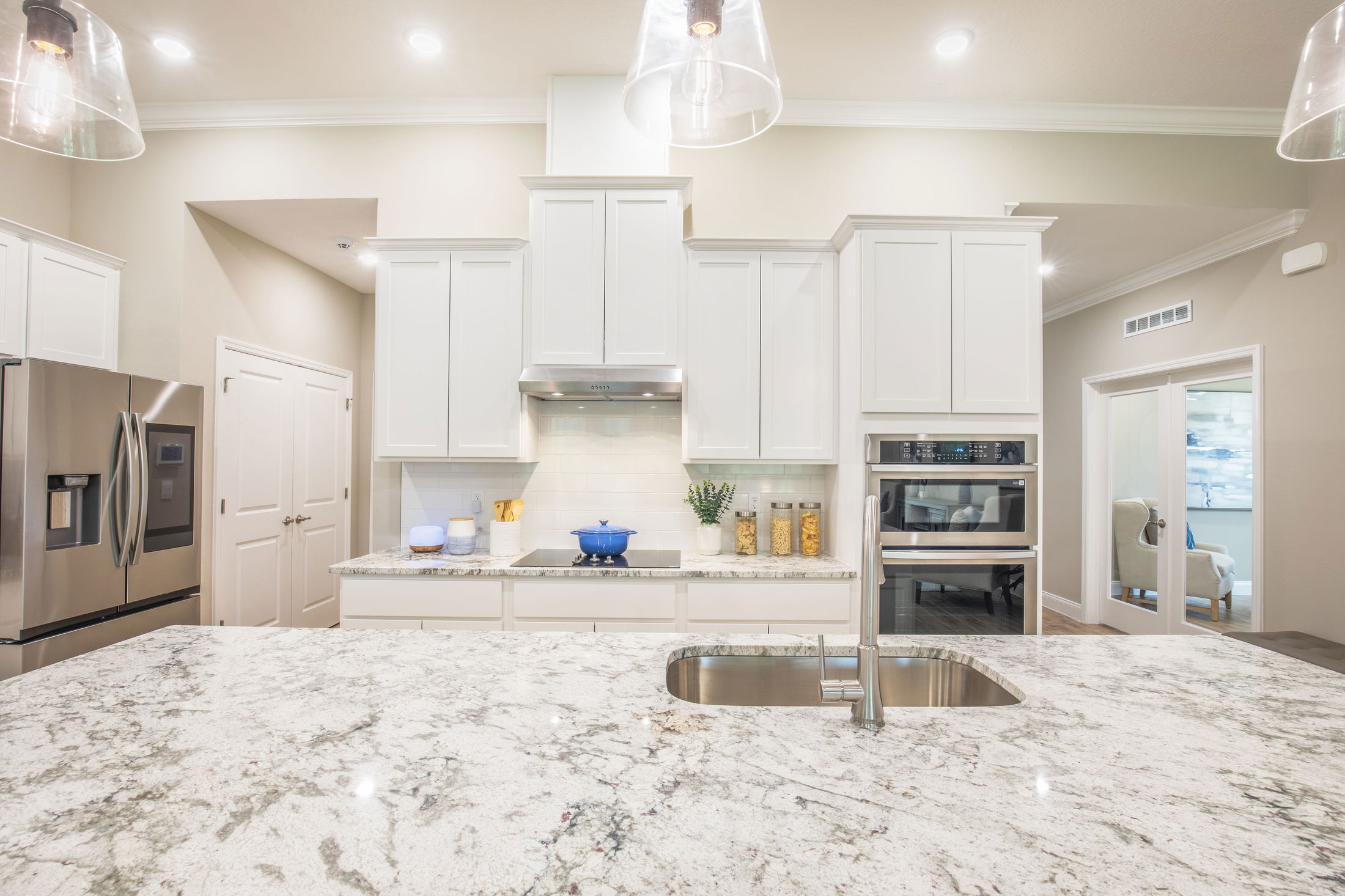 Modern kitchen with white cabinets, stainless steel appliances, marble countertops, and a central island with a built-in sink.