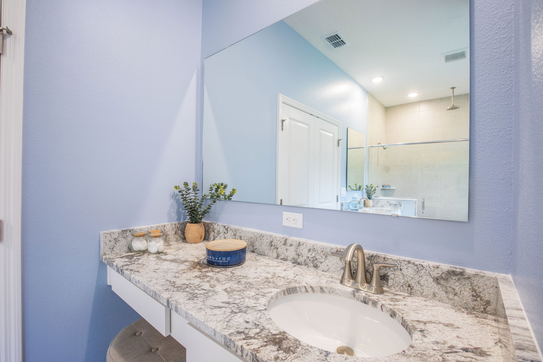 Modern bathroom with a granite countertop, stainless steel faucet, and large mirror reflecting a shower area.