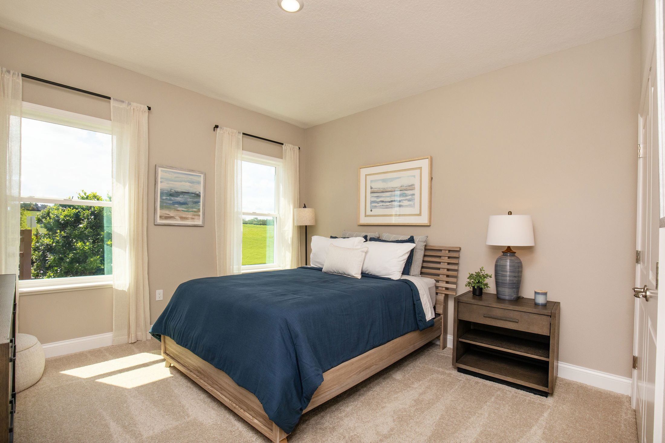 Modern bedroom with a blue-themed decor, featuring a double bed, two windows, and a nightstand with a lamp.