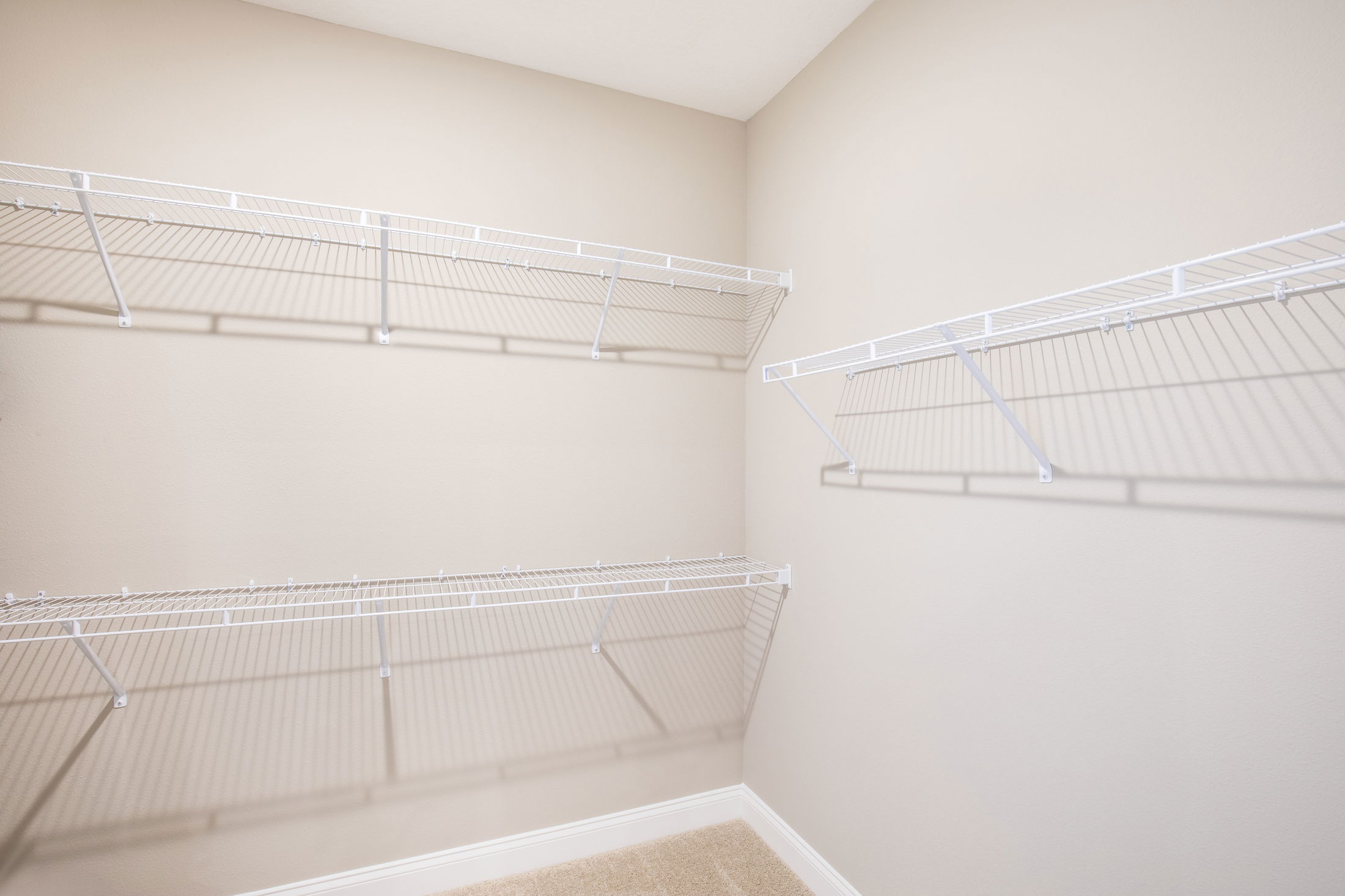 Empty walk-in closet with white wire shelving on beige walls.
