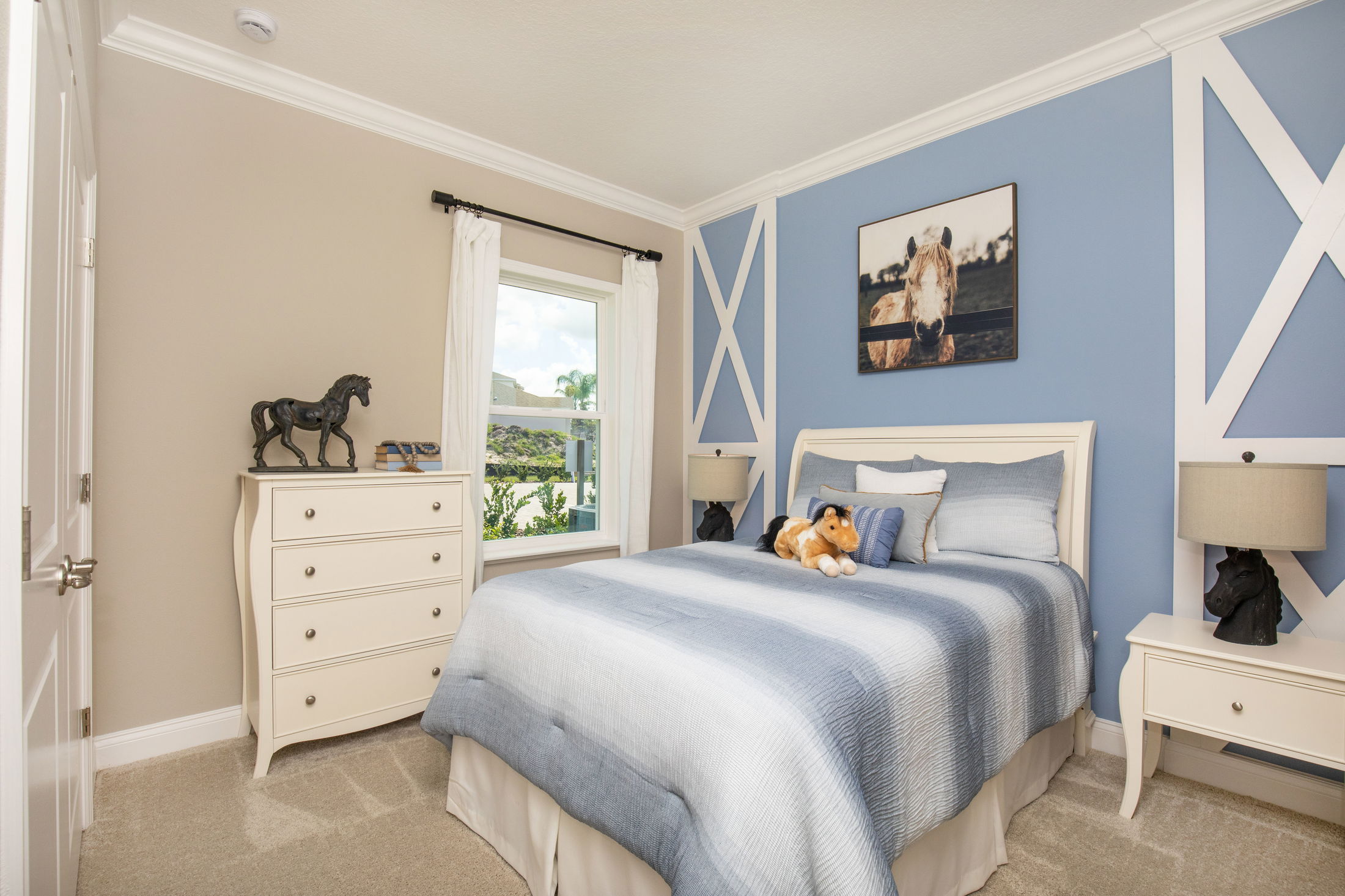 Cozy bedroom with blue and beige decor, featuring a plush horse toy on the bed, horse statue on the dresser, and horse painting above the headboard.