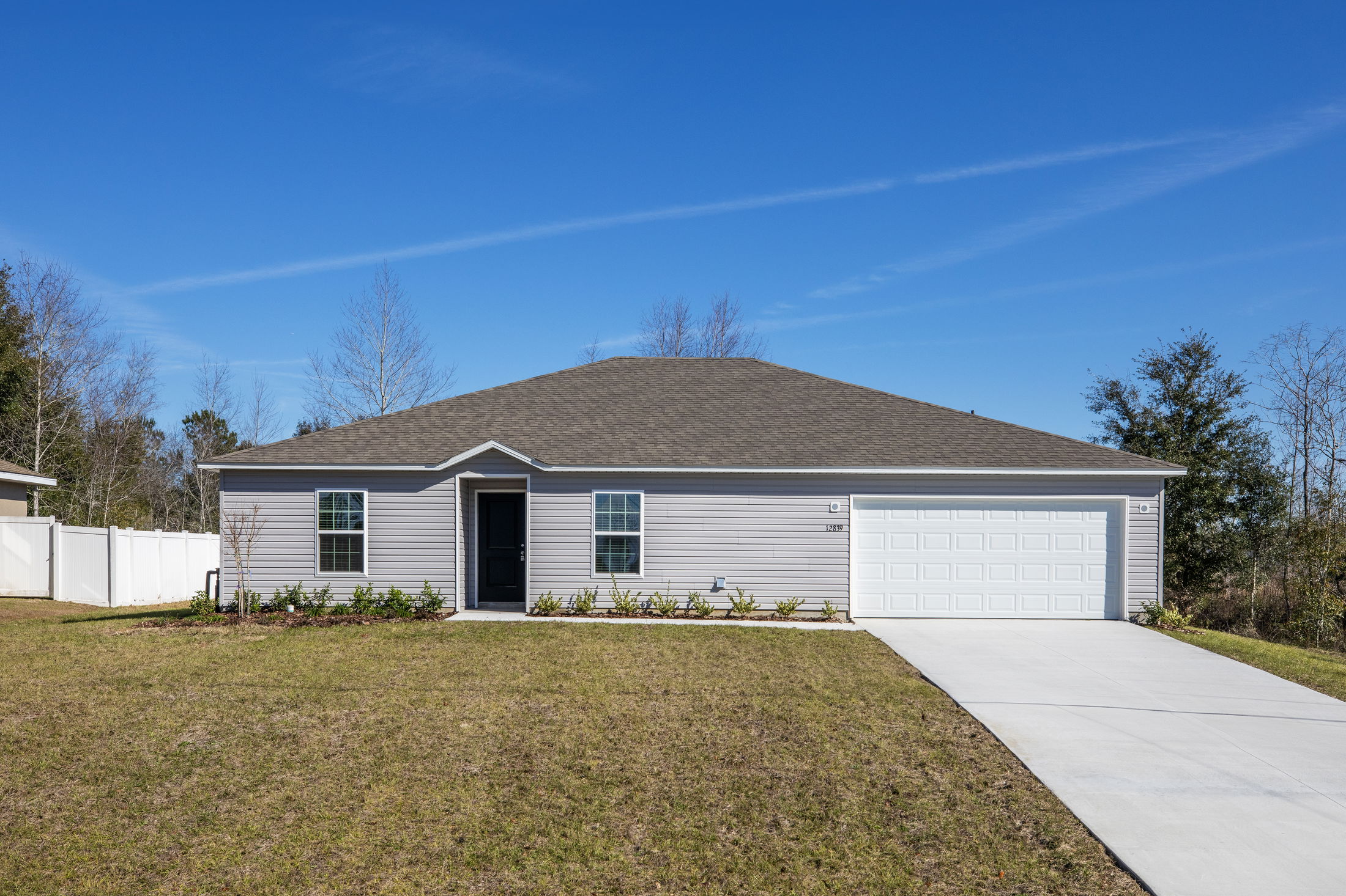Modern single-story gray house with a spacious front yard, white garage door, and clear blue sky.