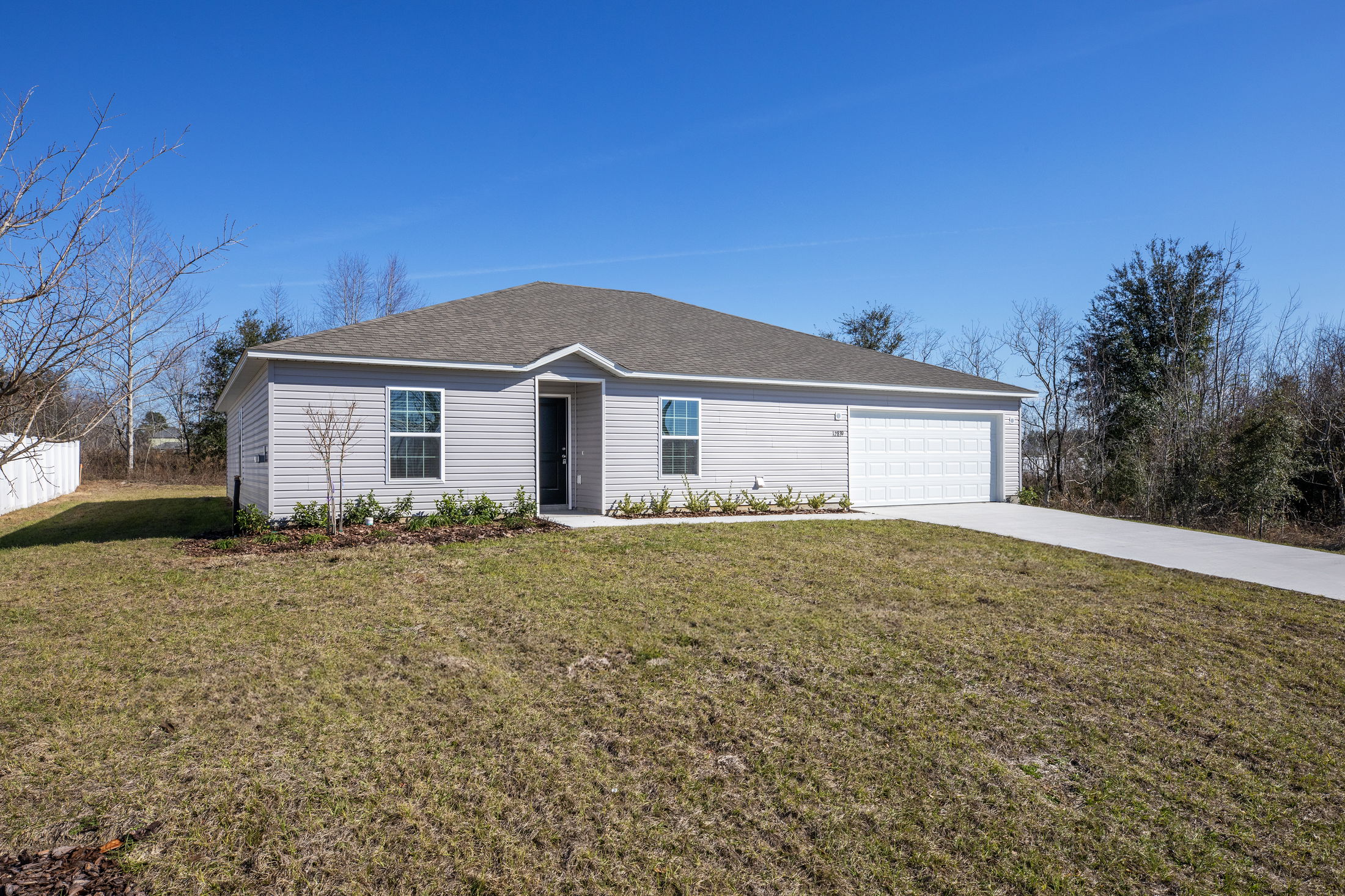 Single-story gray house with attached garage and spacious front yard under a clear blue sky.