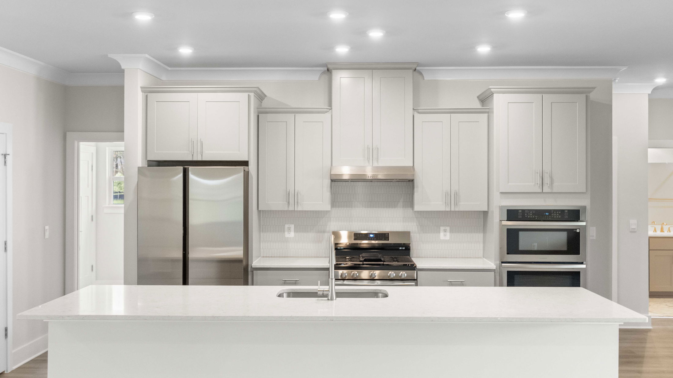 Spacious modern kitchen with white cabinetry, stainless steel appliances, and a central island with a sink.