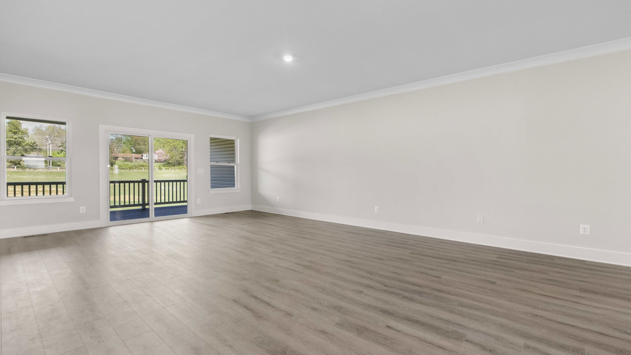 Spacious empty living room with light gray walls, wood flooring, and large sliding glass doors leading to an outdoor view.