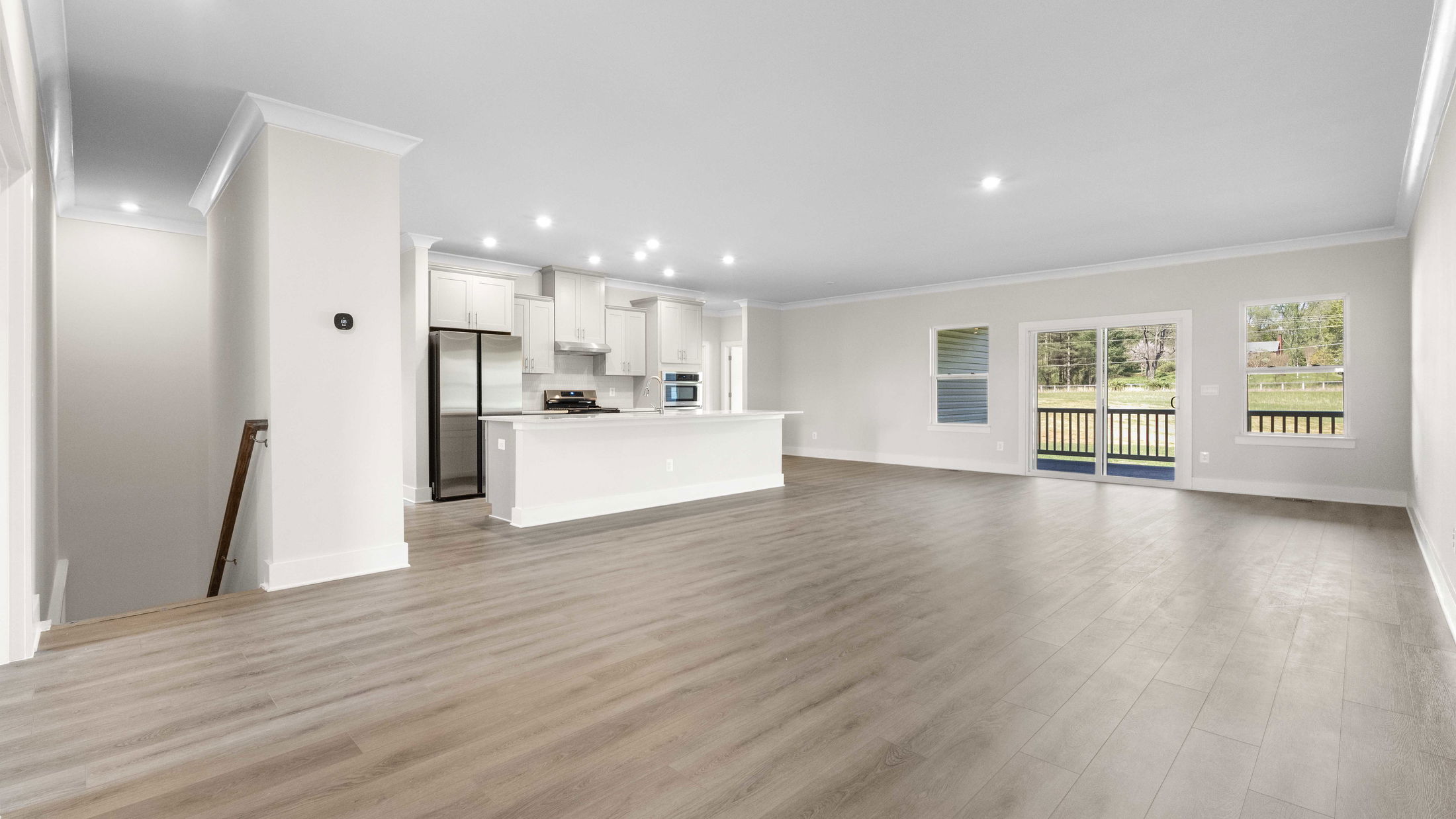 Bright and spacious modern kitchen and living room with hardwood floors, stainless steel appliances, and large windows offering a scenic outdoor view.