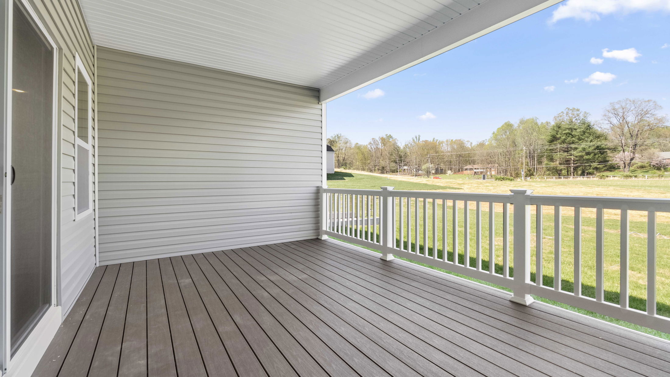 Covered porch with vinyl siding overlooking a grassy field under a clear blue sky.