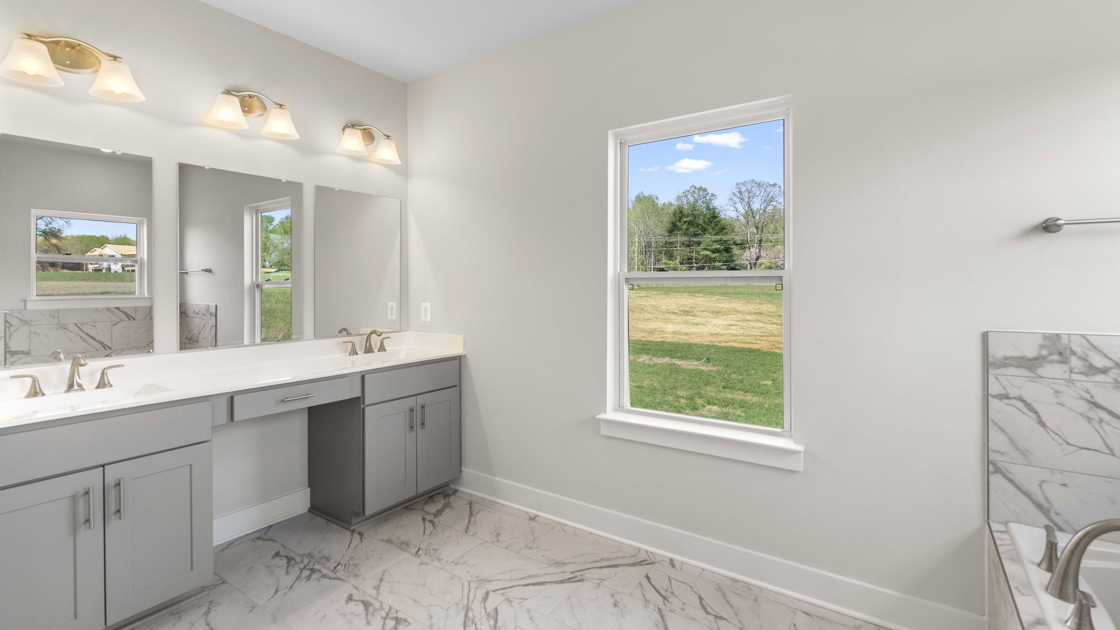 Modern bathroom with double vanity, marble flooring, and a large window showcasing a scenic outdoor view.