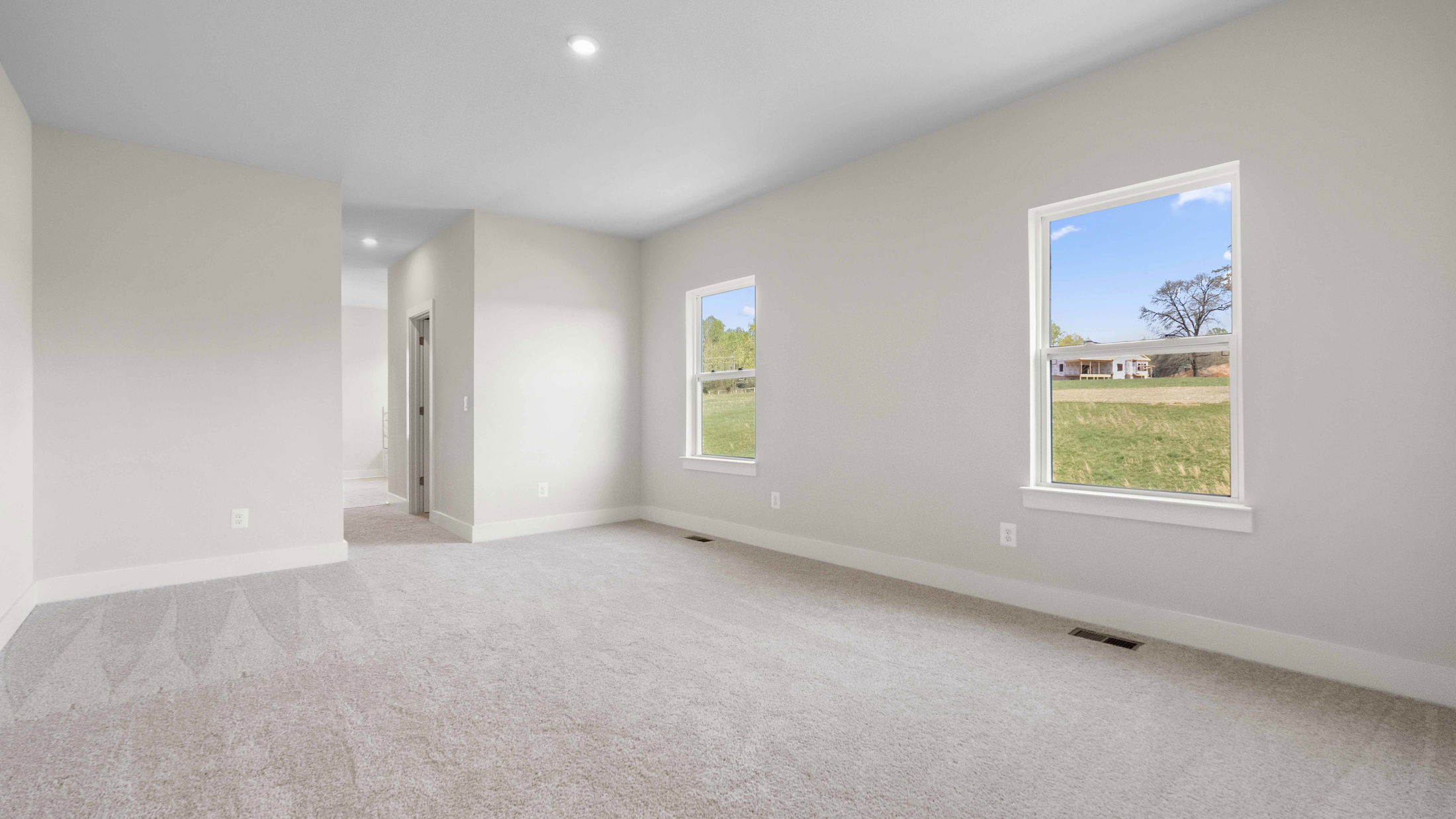 Empty room with beige carpet, two windows, and white walls overlooking a grassy exterior.