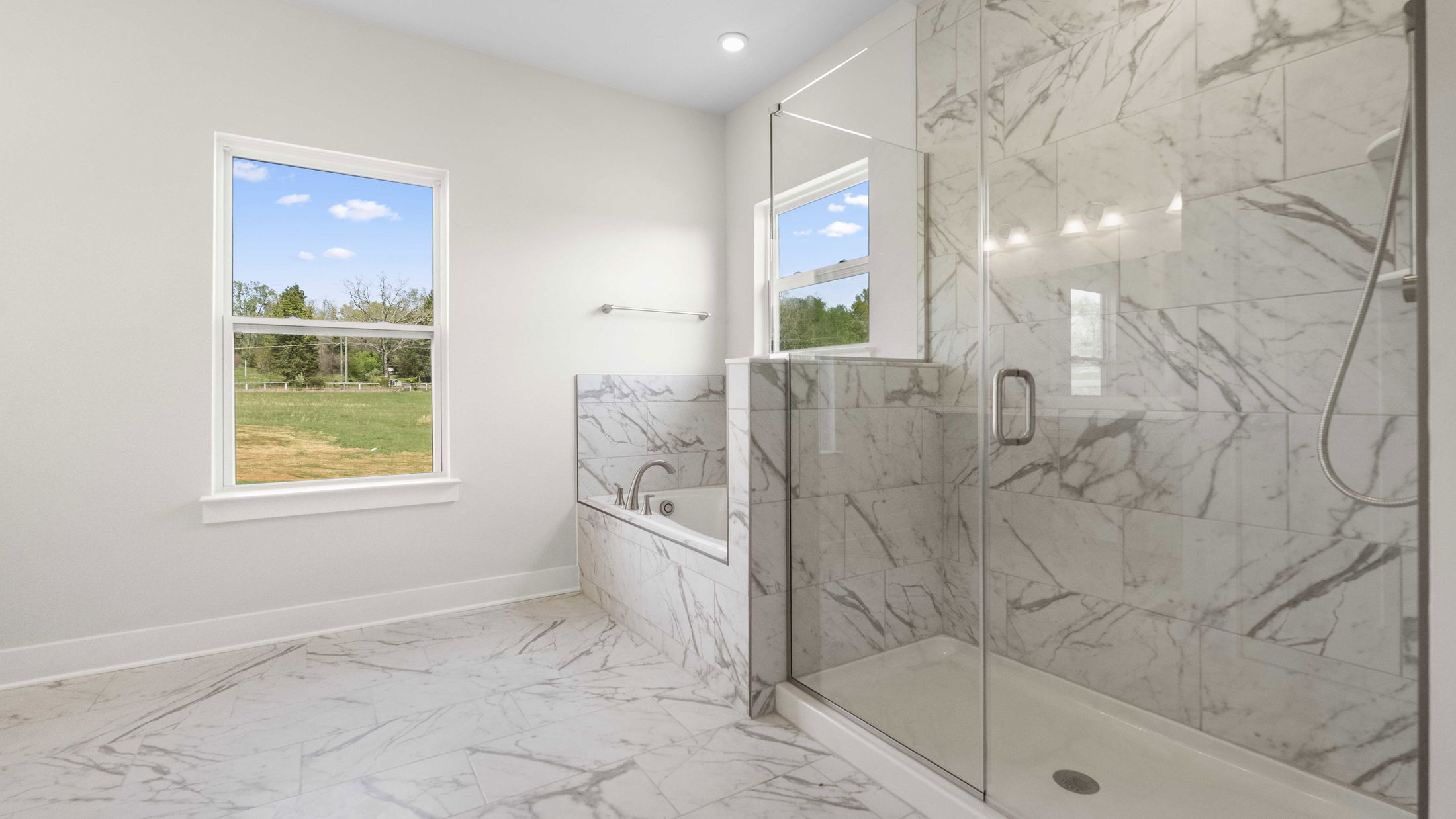 Luxurious bathroom with a glass-enclosed marble shower and bathtub featuring a scenic outdoor view through a large window.