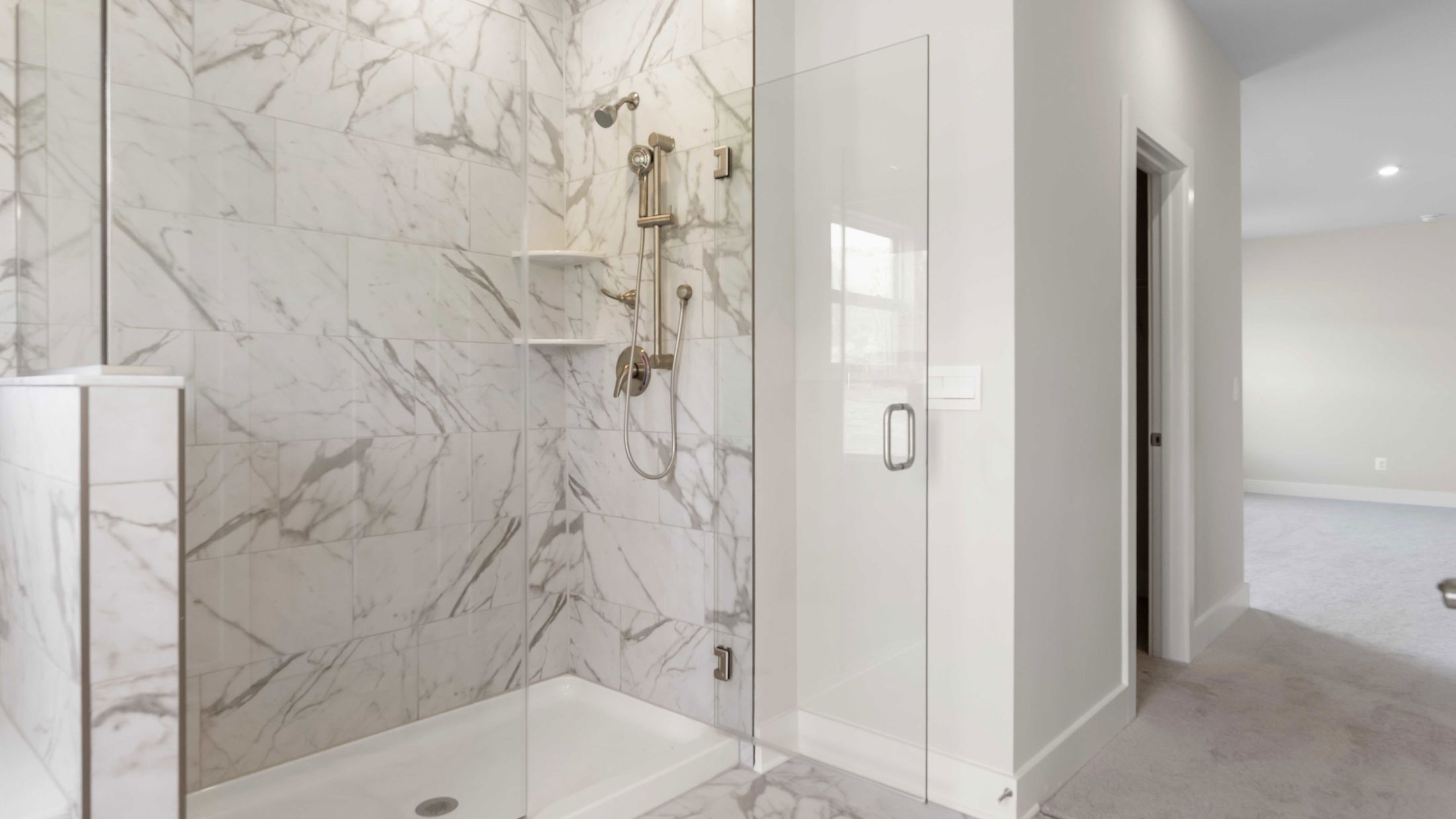 Luxurious marble-tiled bathroom shower with glass door and modern fixtures, capturing a sleek and elegant design.