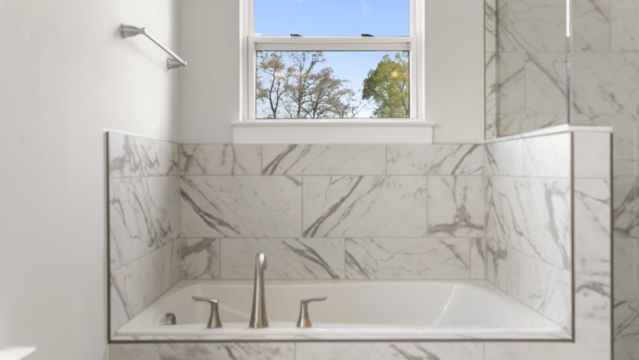 Modern bathroom with a marble-tiled bathtub and a window view of trees.