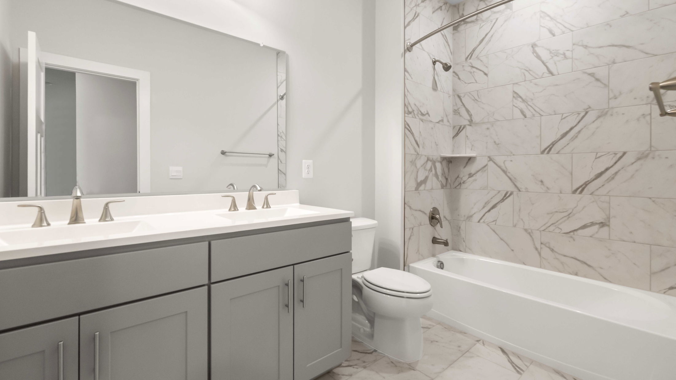 Modern bathroom with gray cabinetry, dual sinks, and a marble-tiled shower and bathtub.