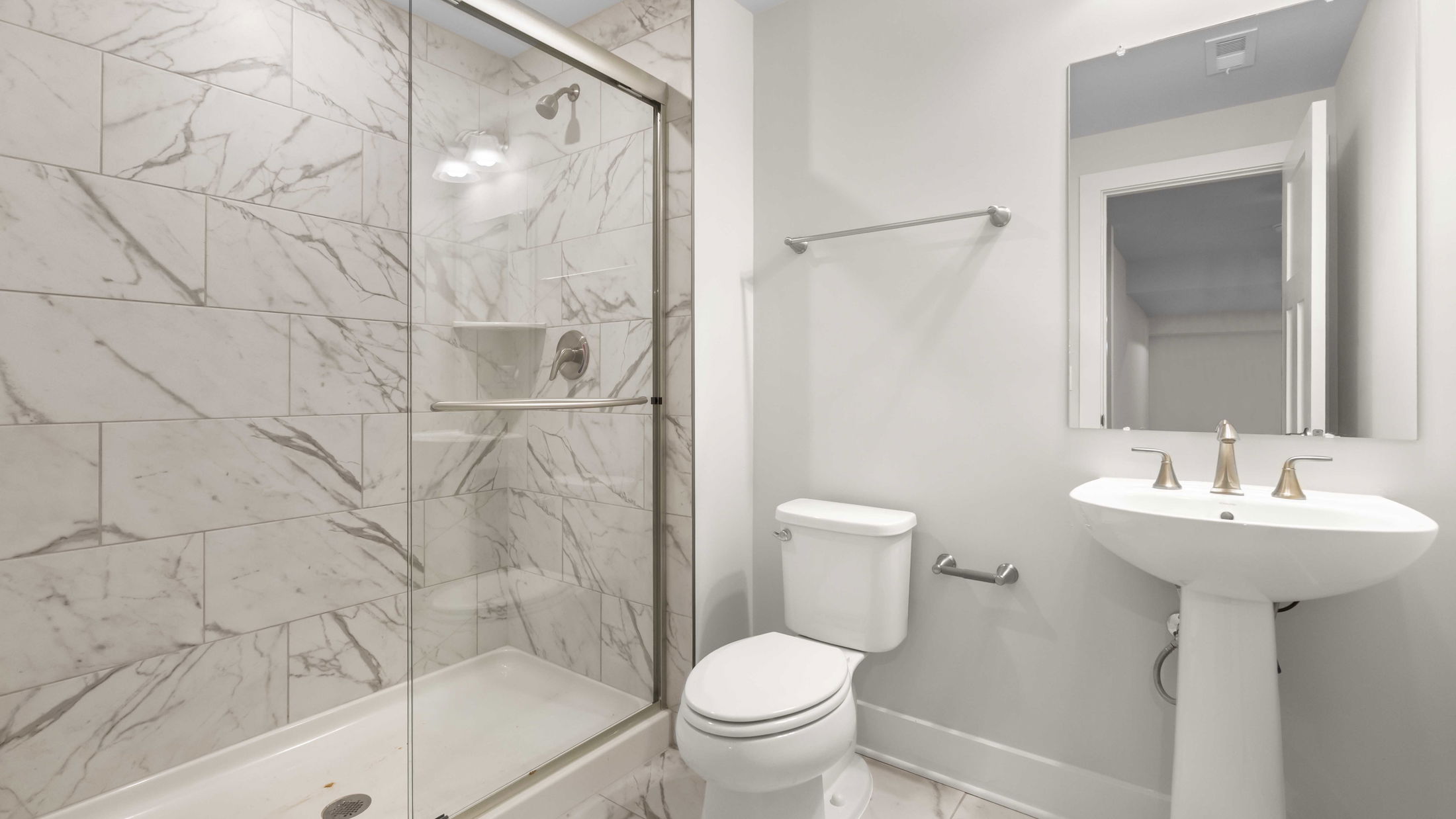 Modern bathroom with marble tile shower, glass doors, white toilet, and pedestal sink.